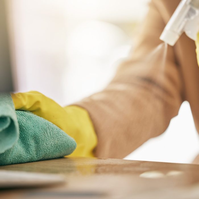 Person, hands and detergent on table with cloth for hygiene, bacteria or germ removal at home. Closeup of cleaner, housekeeper or maid wiping furniture in domestic service or disinfection on surface.